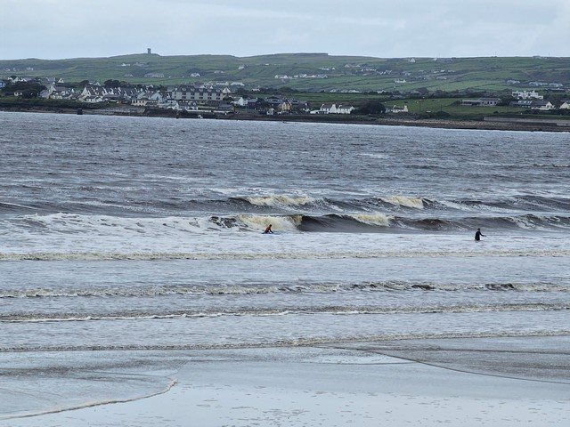 2ft waves breaking as a couple of beginner surfers walk theiir boards deeper 